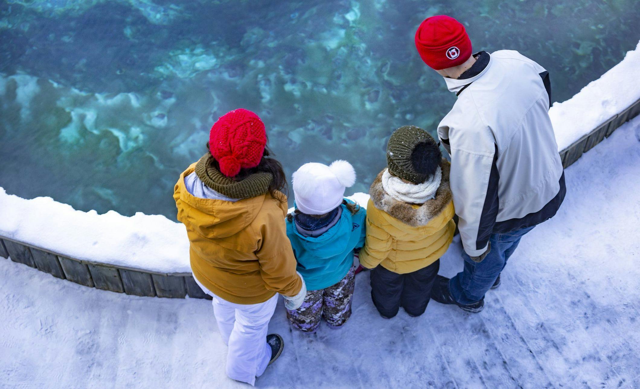 A family of four bundled up for a chilly winter day look into a natural hot spring pool 