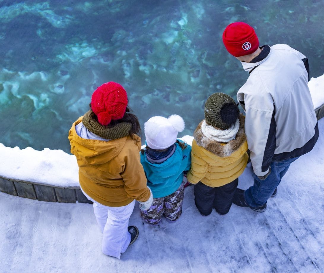 A family of four bundled up for a chilly winter day look into a natural hot spring pool 