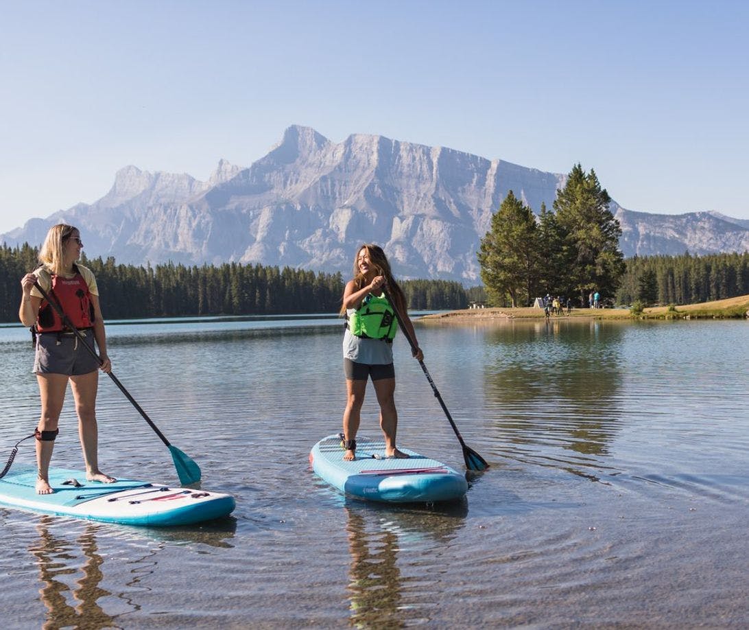 Two people take their stand up paddleboards out on Two Jack Lake at sunrise in Banff National Park in the Canadian Rockies.